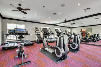 A gym with a variety of equipment including treadmills, elliptical machines, and a fan.